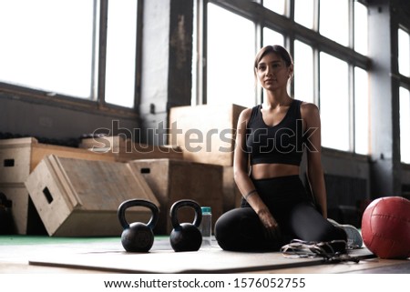 Young woman sitting on floor after her workout and looking down. Female athlete taking rest after fitness training