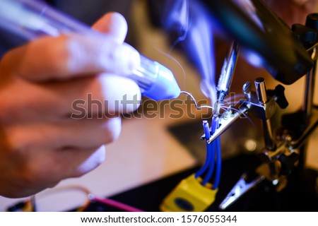 Smoke appears while soldering ESC and rotor wires with helper hands. Technology and electrical engineering concept. Autonomous vehicles like drones need a lot of soldering in building process Royalty-Free Stock Photo #1576055344