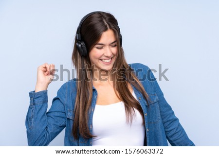 Teenager Brazilian girl listening music and dancing over isolated blue background