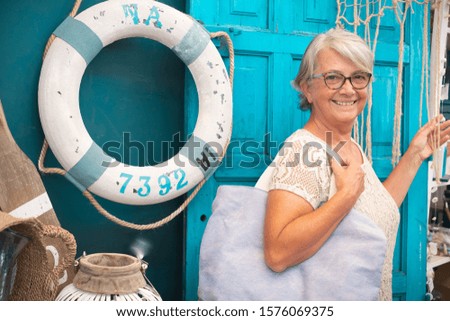 Happy Senior pretty lady with gray hair looking at camera. Romantic and rustic corner with blue door in background. Navy style accessories.