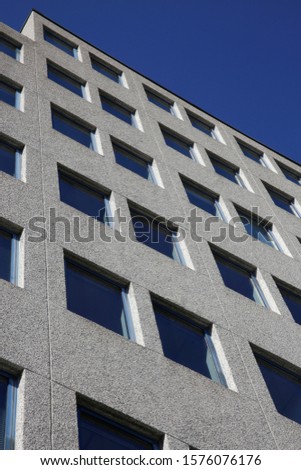 Contrast low-angle photo of high-rise building. Modern architecture image with perspective. Urban real estate. Diagonal composition of concrete facade wall with windows under bright blue sky.