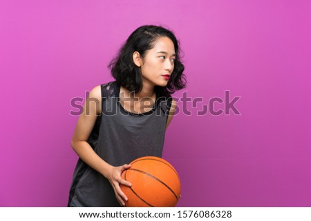 Young Asian woman playing basketball over isolated purple background