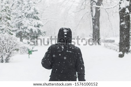Man in black jacket walking in the street in cold snowy winter day.