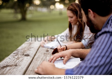 A closeup shot of people sitting in the park and reading the bible with a blurred background
