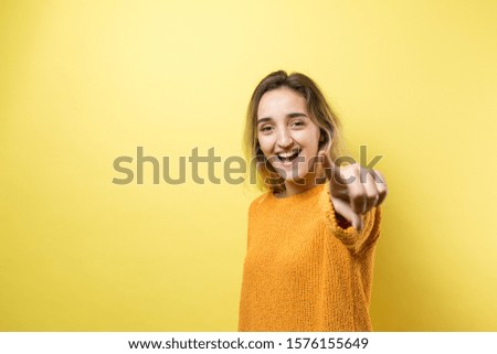 Happy young caucasian female in an orange sweater pointing fingers away	
