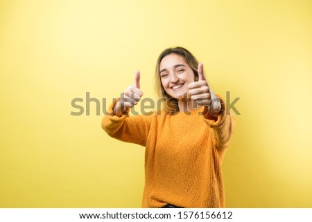 Happy young caucasian female in an orange sweater making thumb up sign and smiling. Good job and respect.	
