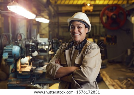 Waist up portrait of mixed-race female worker posing confidently while standing with arms crossed in factory workshop Royalty-Free Stock Photo #1576172851