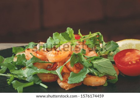 Fresh homemade salad of shrimp, arugula and tomato on a black slate dish, close-up