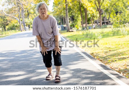 Asian senior woman is extremely tired while walking at park, body is weak feeling tired easily due to lack of energy and don’t exercise very often, exhausted elderly people have the symptoms fatigue Royalty-Free Stock Photo #1576187701