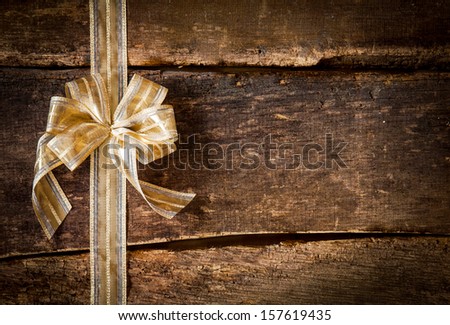Festive ornamental gold ribbon and bow on a grunge rustic wood background with copyspace for your Christmas, anniversary or birthday wishes