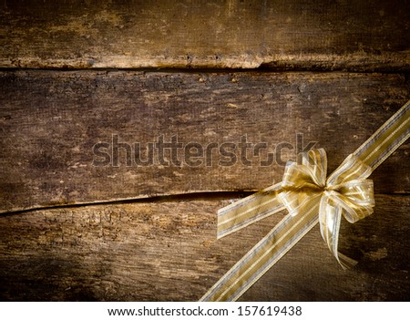 Dainty gold bow arranged diagonally in the corner on a rustic wood background of old dark textured planks with copyspace for seasonal Christmas text