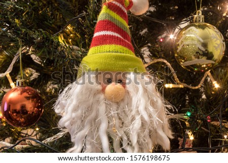 Closed Up to Santa Claus on christmas tree with white beard and green & red wool cap. with christmas red and gold balls, and multicolor lights