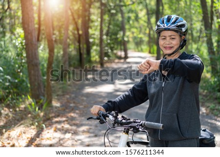 Senior asian woman bicycle in the park, With checking time or heart rate from smart watch 