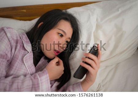 cozy lifestyle portrait of young beautiful and sweet Asian Chinese woman in cute pajamas  playful in bed using mobile phone enjoying social media or online dating app happy and relaxed 