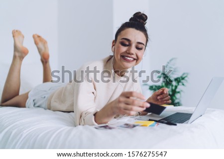 Attractive pensive young woman relaxing on bed with laptop photo or credit card thinking and smiling on white wall background