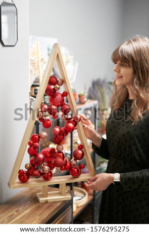 Alternative wooden christmas tree in womans hands . A handmade Christmas tree and red christmas balls.