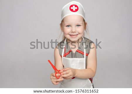 Pretty little girl in doctor's uniform with scissors.