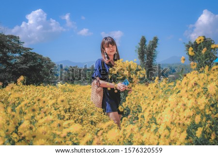 Woman holding a bouquet of flowers standing in a field of yellow chrysanthemum.