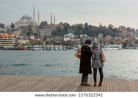 Two young women tourists walk and take pictures in the coastline of Karakoy district in Istanbul