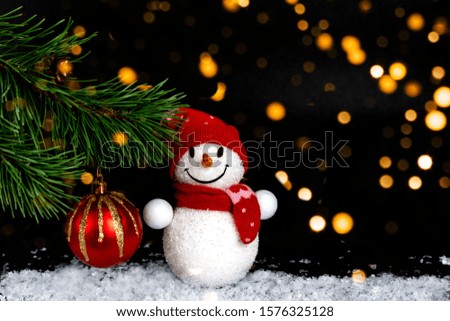 Snowman toy, Christmas balls, background with fir branch, on a black festive background with lights of lanterns and falling snow. Merry Christmas and Happy New Year greeting card with copy space.
