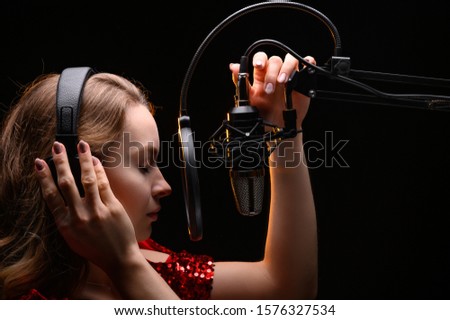 The vocalist sings in the studio in a studio microphone. In headphones, on a black background. Artist, recording an album, disc. Working with the label