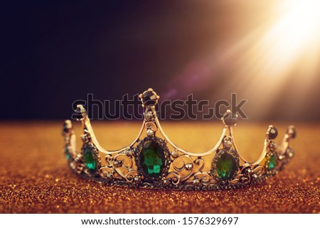 low key image of beautiful queen/king crown over gold glitter table. vintage filtered. fantasy medieval period Royalty-Free Stock Photo #1576329697