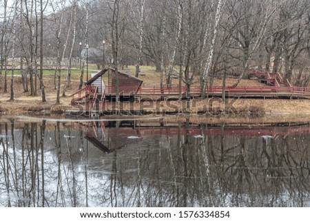 Trees and a house on the shore of the pond are reflected on the first ice of the frozen pond in the city Park