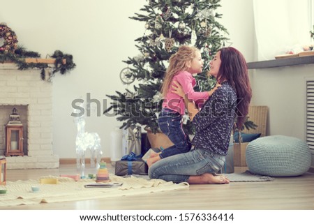 Mom and daughter are hugging while sitting on the floor under the Christmas tree. Christmas morning. Good time at home.