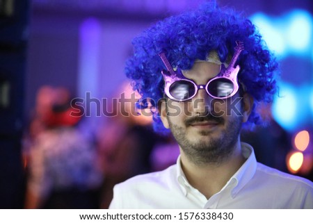 Young man wearing a blue toupee during the eighties party.