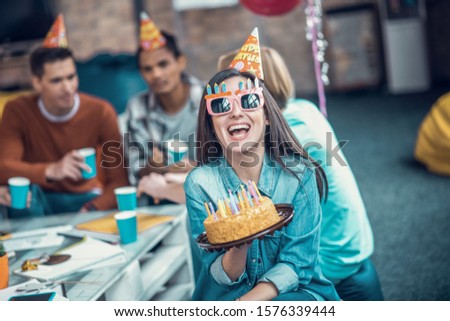 Holding birthday cake. Beautiful girl wearing glasses smiling while holding birthday cake and having party