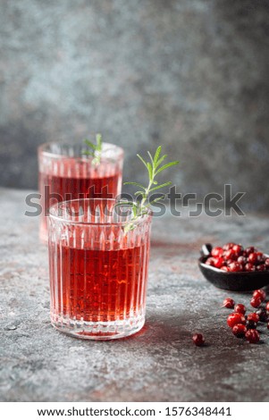 Fresh cranberry cocktail with rosemary in a glass on gray background.