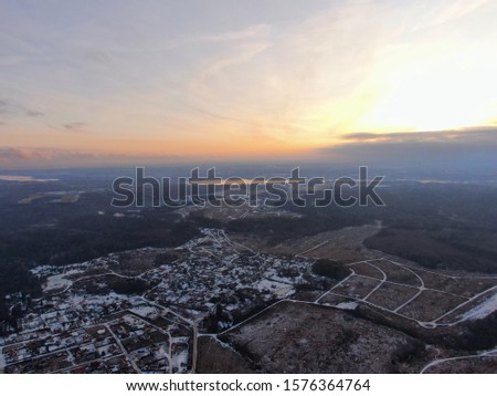 Aerial view green field surrounded by forest covered with white snow. Beautiful panoramic landscape of nature