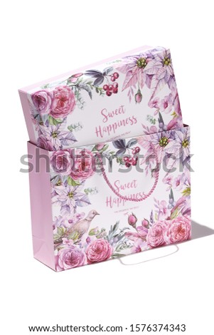 Subject shot of a gift box in a gift bag with plaited handles. Both items are decorated with floral tropic print, design with letters and a pleasant text: "Sweet happiness. You deserve the best."