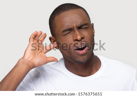 Unhappy African American man with closed eyes and open mouth plug finger in ear, feeling pain, upset young male suffering from earache, health problem, loud noise, isolated on studio background Royalty-Free Stock Photo #1576375651