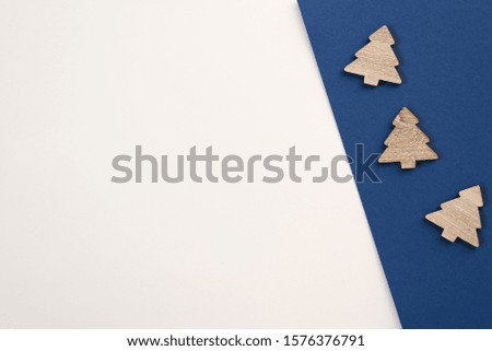 Creative minimalistic postcard with copy space. Decorative wooden Christmas trees on colored white and blue background