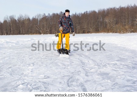 Teenager brush snow with shovel on ice of forest lake for ice skating. Healthy lifestyle.