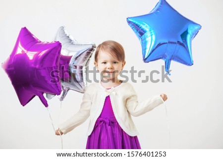 Little baby girl holding balloons in the form of stars. Young girl holding a star-shaped balloons. Happy child with colorful shiny foil balloons against a white background