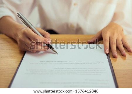 Woman signing document and hand holding pen putting signature at paper, order to authorize their rights.