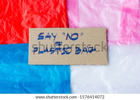 Hand written text "say no to plastic bag" on a piece of cardboard placing over colorful texture of single use plastic bags. Pollution concept.
