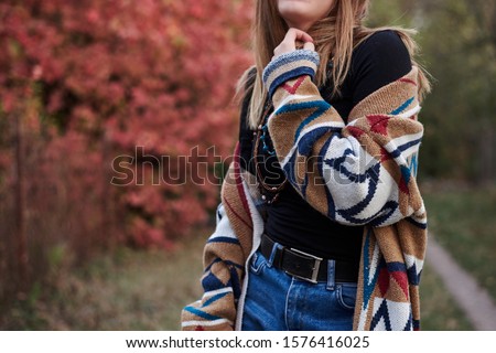 Close-up portrait of young blond woman's body jumping dancing in autumn park, woods. Young girl, wearing blue jeans and colorful cardigan, posing in forest, having fun. Hippie style. Royalty-Free Stock Photo #1576416025