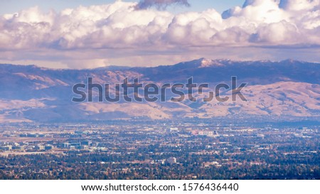 Aerial view of Santa Clara and South San Jose, Silicon Valley, San Francisco Bay Area, California; Diablo mountain range with a dusting of snow covering the peaks visible in the background; cloudy sky