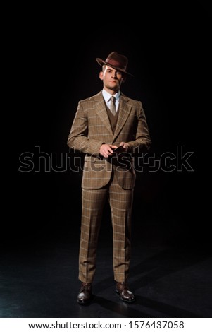 stylish man in hat holding smartphone on black  Royalty-Free Stock Photo #1576437058