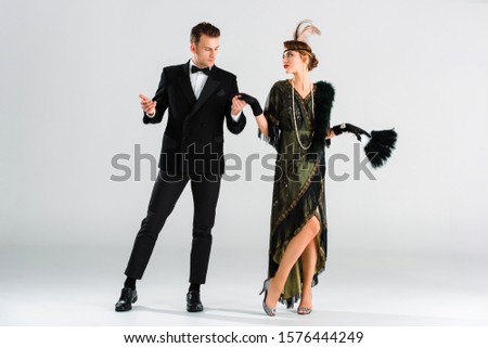 stylish man in suit and aristocratic woman holding hands while dancing on grey Royalty-Free Stock Photo #1576444249