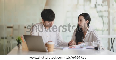 Two young professional graphic designer working on their project together with laptop computer in modern office room 