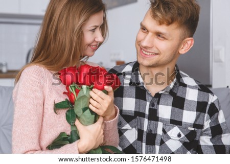 Young man and woman family sitting together on the coach having date wife holding red roses looking on her husband smiling