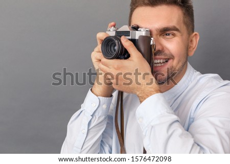 Young man studio standing isolated on grey background taking photos on gilm camera smiling joyful close-up photography hobby