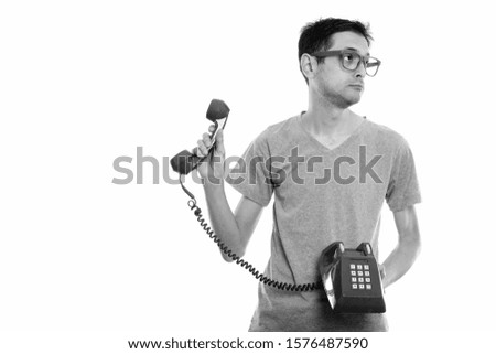 Studio shot of young man holding old telephone and looking away