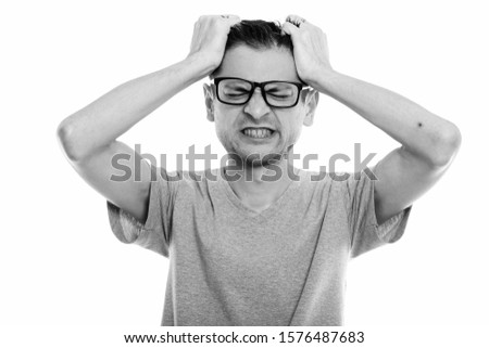 Studio shot of angry young man wearing eyeglasses while pulling his hair