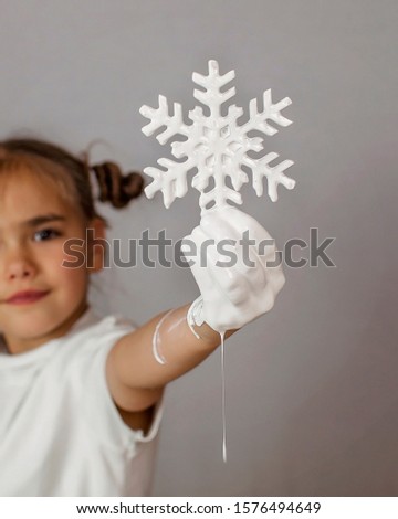 Cute girl with white painted hand holding a white colored snowflake, color melting down the arm, trendy abstract studio shot isolated over white background. Ecology problem and global warming concept
