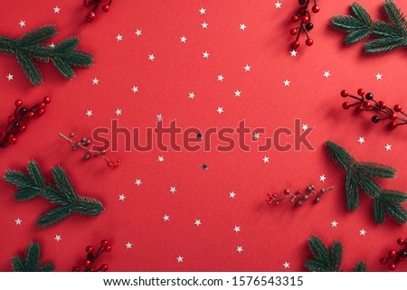 Christmas minimal concept - christmas tree branch on red background with red berrie and star silver confetti. Creative minimal. Christmas greeting card design template. Holiday frame.